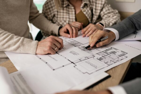 Close-up of people reviewing a custom home floor plan with hands pointing at layout details during a construction planning meeting.