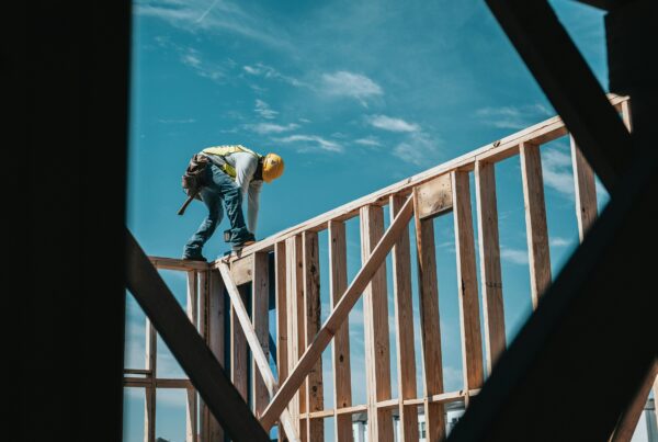 A construction worker wearing safety gear stands on a wooden home frame, working on new home construction.