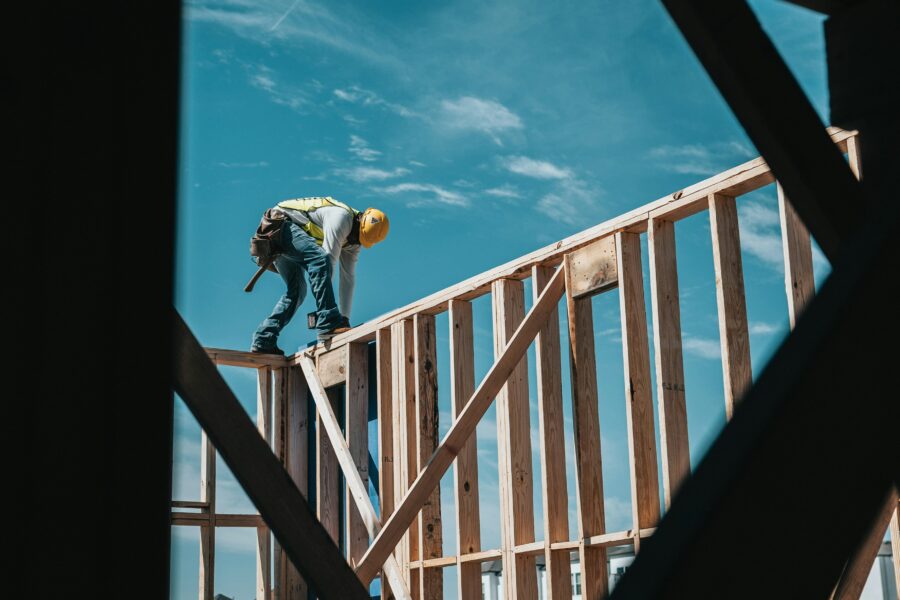 A construction worker wearing safety gear stands on a wooden home frame, working on new home construction.