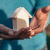 A person holding a small wooden house in their hands, symbolizing building a custom home.