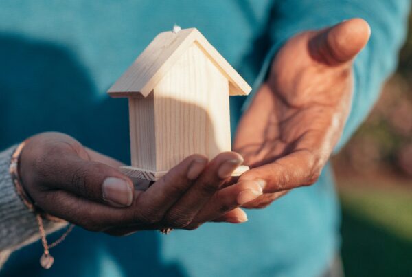 A person holding a small wooden house in their hands, symbolizing building a custom home.